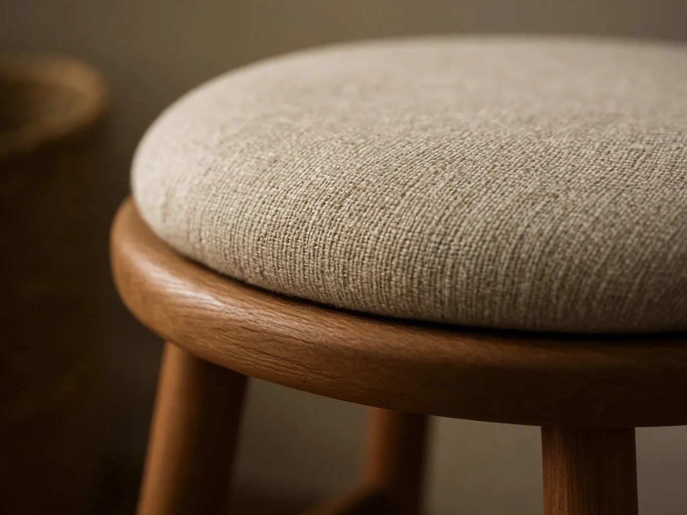 Close-up of a beige upholstered stool seat with a wooden frame against a soft blurred background